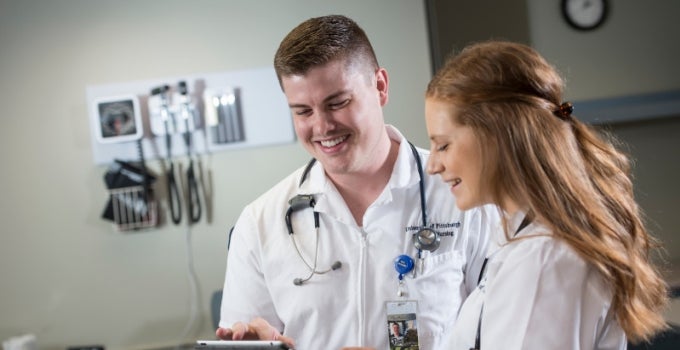 two smiling nursing students looking at a tablet