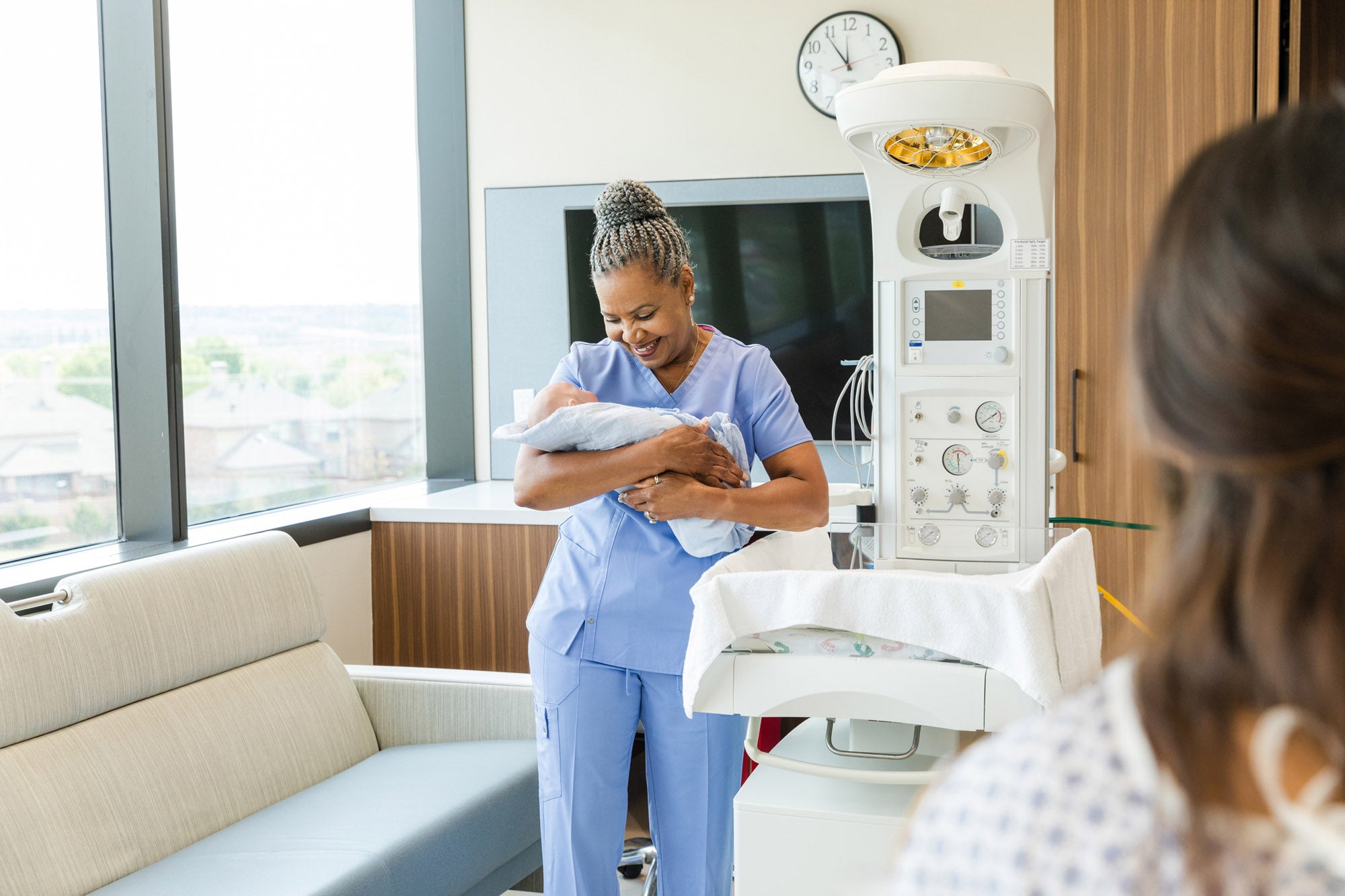 A smiling nurse gently cradles a newborn infant in a hospital setting.