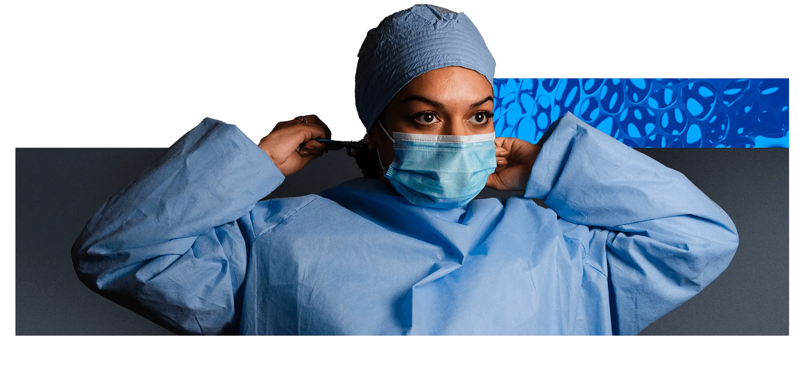 Female nurse in scrubs and cap secures surgical mask over her face
