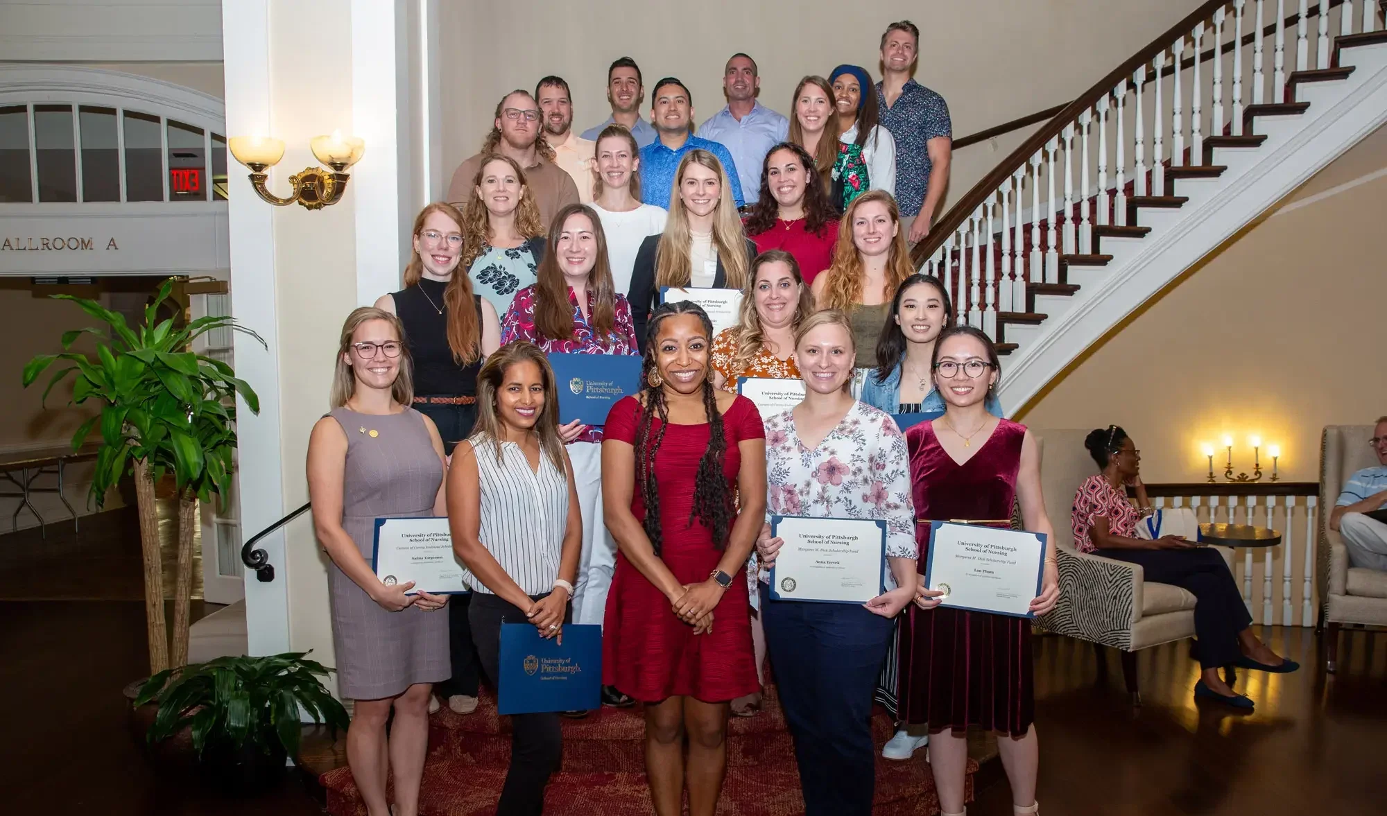 Group of smiling nursing alumni stand on a spiral staircase holding certificates