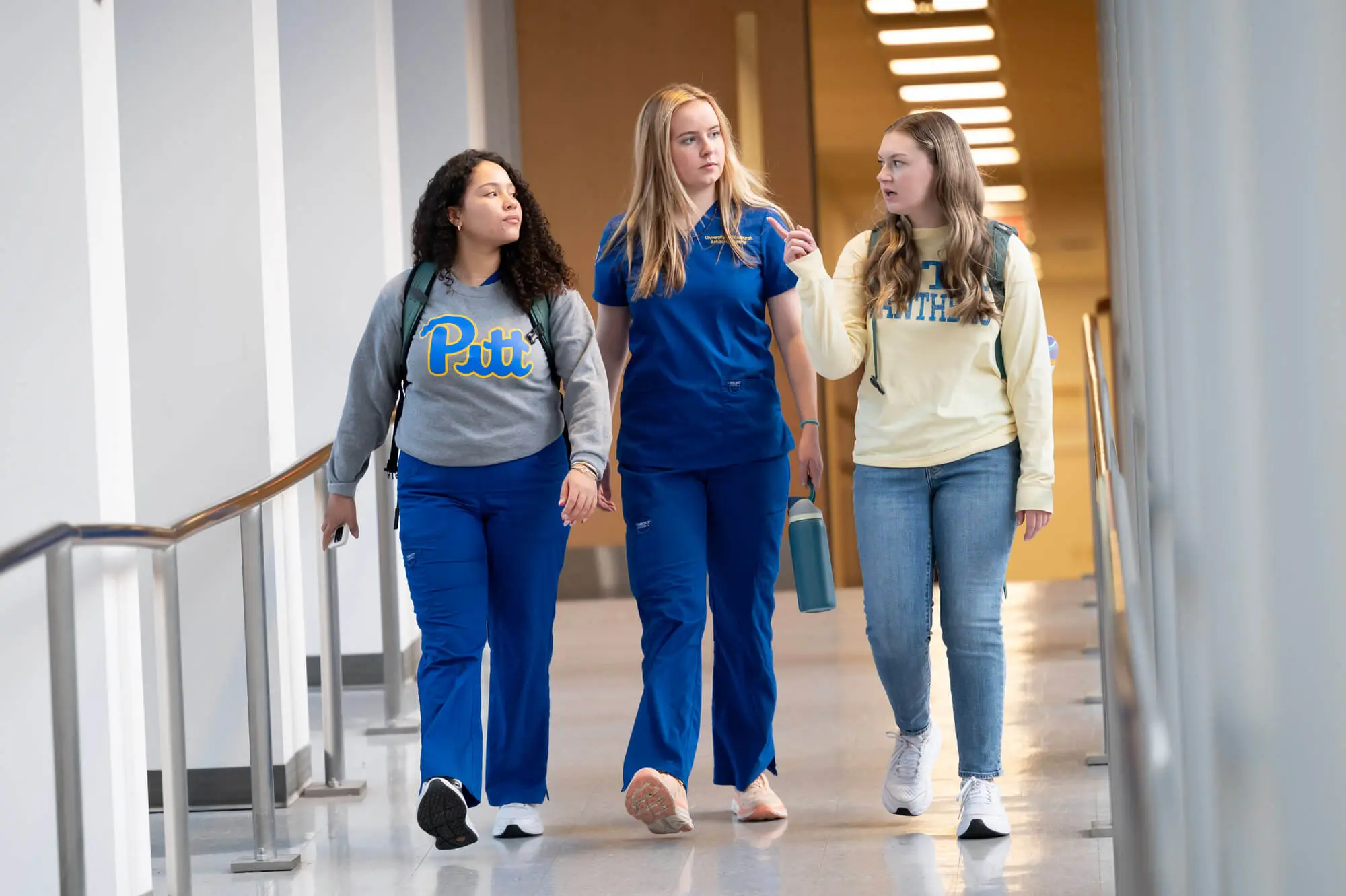 Three nursing students walk down a hall together, talking.