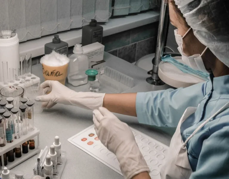 Nurse in protective gear wearing white hospital gloves handles medical samples